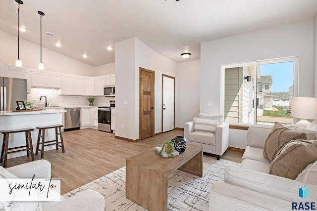 living room featuring light hardwood / wood-style floors, vaulted ceiling, and sink