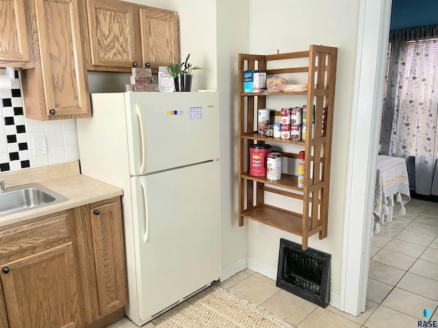 kitchen with white refrigerator, light tile patterned floors, sink, and backsplash