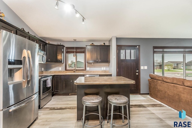 kitchen featuring appliances with stainless steel finishes, light wood-type flooring, sink, pendant lighting, and a center island