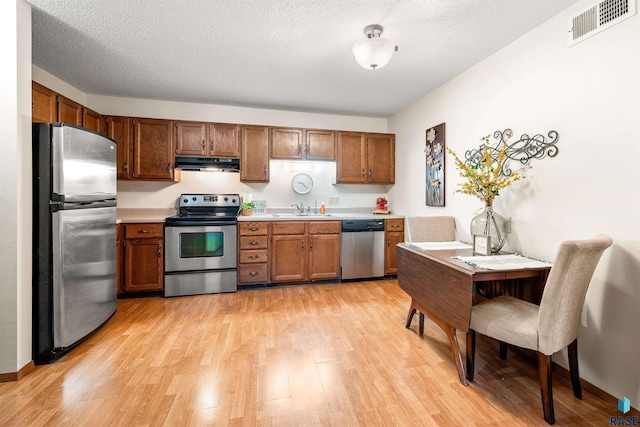 kitchen with sink, stainless steel appliances, a textured ceiling, and light wood-type flooring