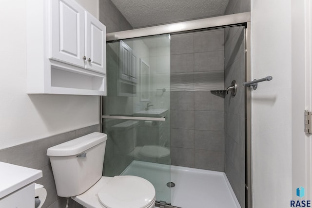 bathroom with vanity, toilet, a textured ceiling, tile walls, and a shower with shower door