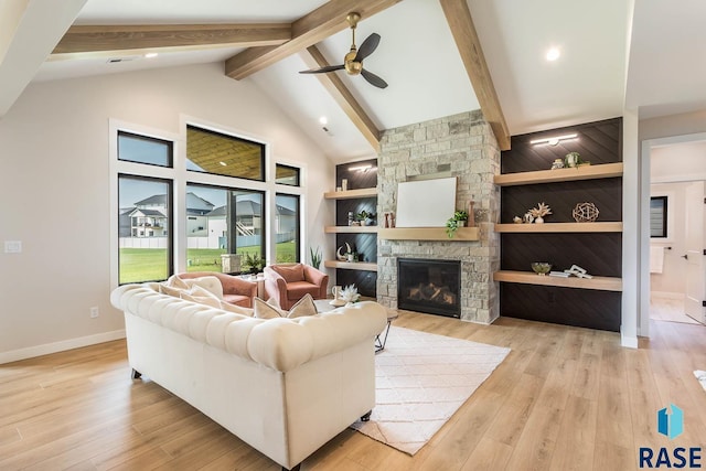 living room with built in shelves, ceiling fan, a stone fireplace, and light hardwood / wood-style floors