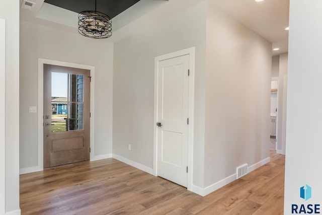 entryway featuring light hardwood / wood-style floors, a raised ceiling, and an inviting chandelier