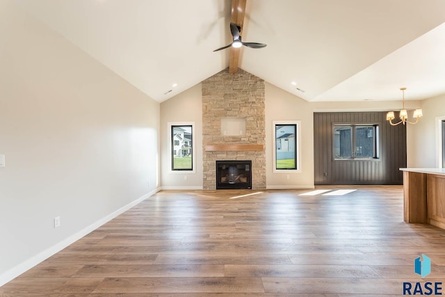 unfurnished living room with a fireplace, lofted ceiling with beams, ceiling fan with notable chandelier, and hardwood / wood-style flooring