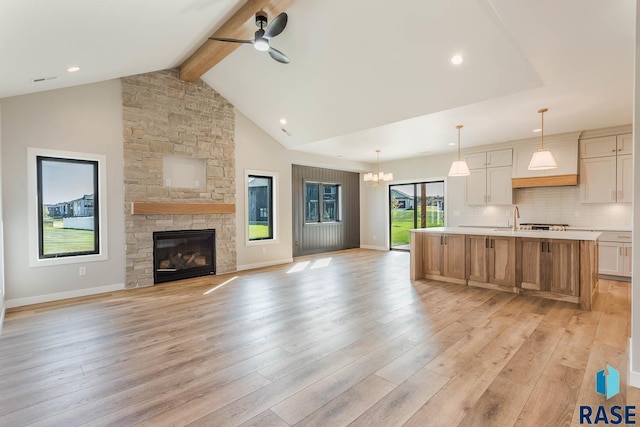 unfurnished living room with ceiling fan with notable chandelier, sink, light hardwood / wood-style flooring, a fireplace, and beam ceiling