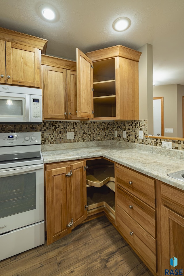 kitchen with light stone countertops, dark hardwood / wood-style flooring, tasteful backsplash, white appliances, and sink