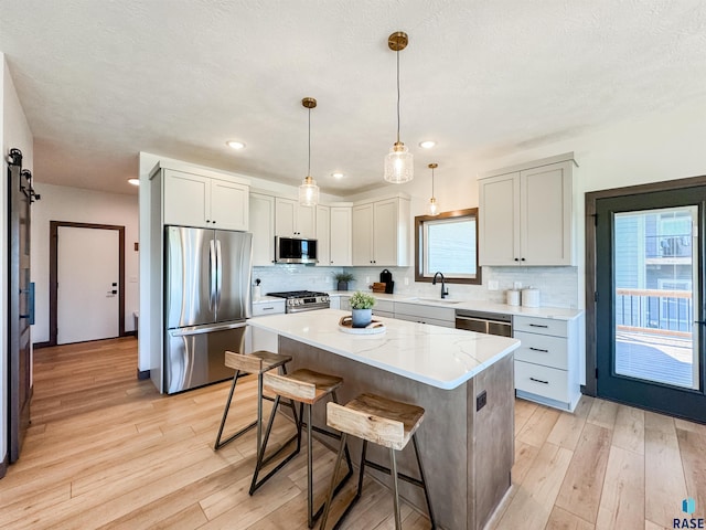 kitchen featuring tasteful backsplash, a barn door, appliances with stainless steel finishes, a sink, and a kitchen bar