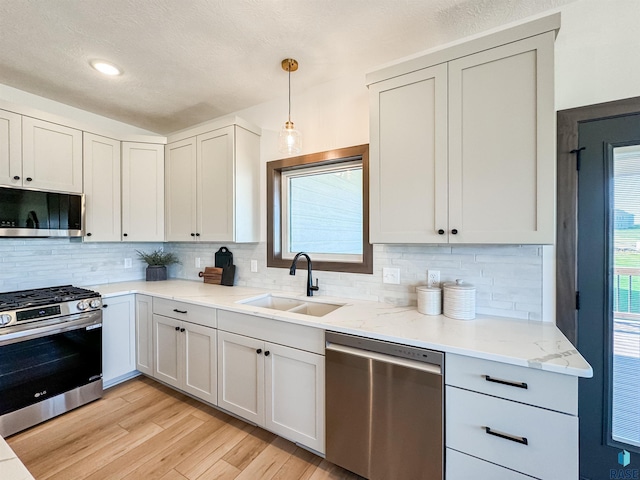 kitchen featuring stainless steel appliances, light wood finished floors, a sink, and decorative backsplash