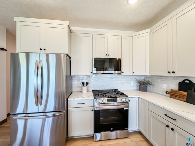 kitchen featuring light stone counters, backsplash, appliances with stainless steel finishes, light wood-style floors, and a textured ceiling