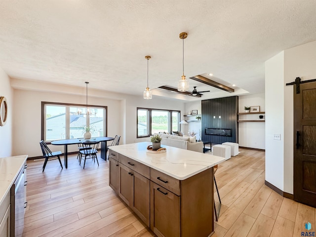 kitchen with light stone counters, pendant lighting, a barn door, light wood-style floors, and a kitchen island