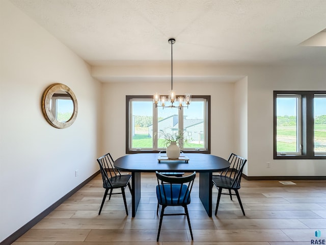 dining space featuring a textured ceiling, visible vents, baseboards, light wood finished floors, and an inviting chandelier