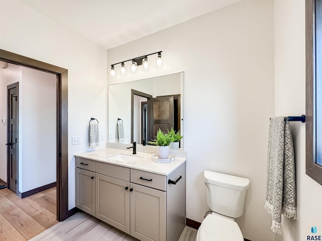 bathroom with vanity, wood finished floors, toilet, and baseboards