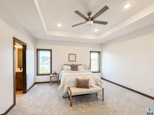 bedroom featuring recessed lighting, light carpet, baseboards, a tray ceiling, and ensuite bath