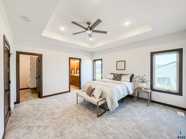 bedroom featuring light carpet, baseboards, multiple windows, and a tray ceiling