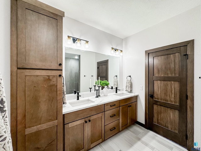 bathroom with double vanity, a sink, and tiled shower