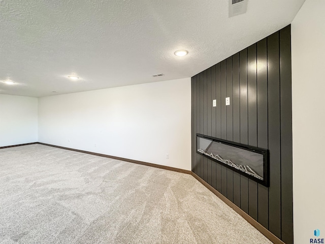 carpeted spare room featuring a textured ceiling, a large fireplace, visible vents, and baseboards