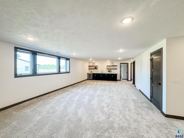 unfurnished living room with baseboards, a textured ceiling, and light colored carpet