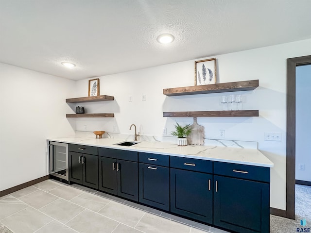 bar featuring beverage cooler, a textured ceiling, a sink, and baseboards