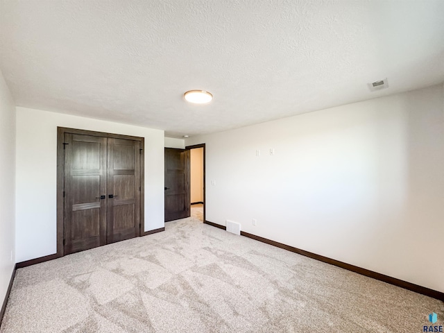 unfurnished bedroom featuring a textured ceiling, light colored carpet, visible vents, baseboards, and a closet