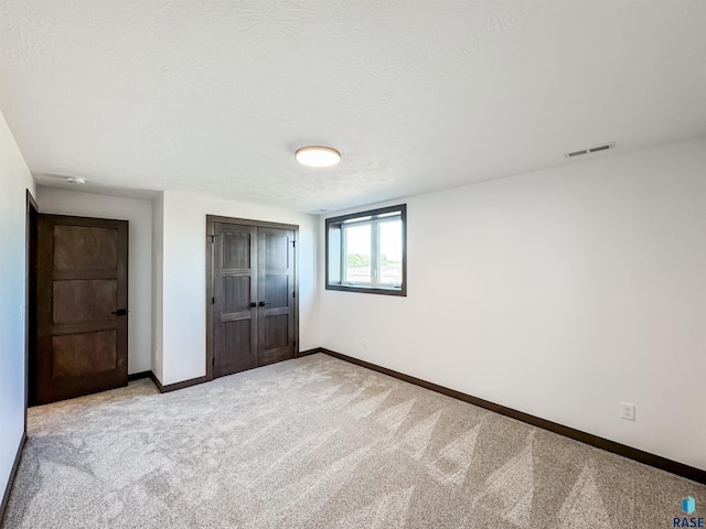 unfurnished bedroom with baseboards, visible vents, light colored carpet, a textured ceiling, and a closet