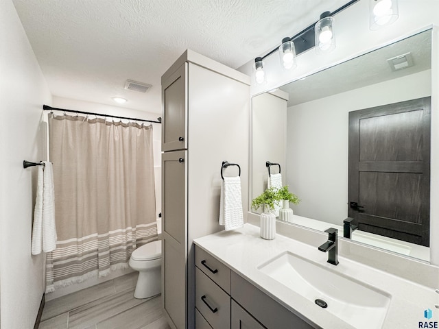 full bathroom featuring visible vents, vanity, toilet, and a textured ceiling