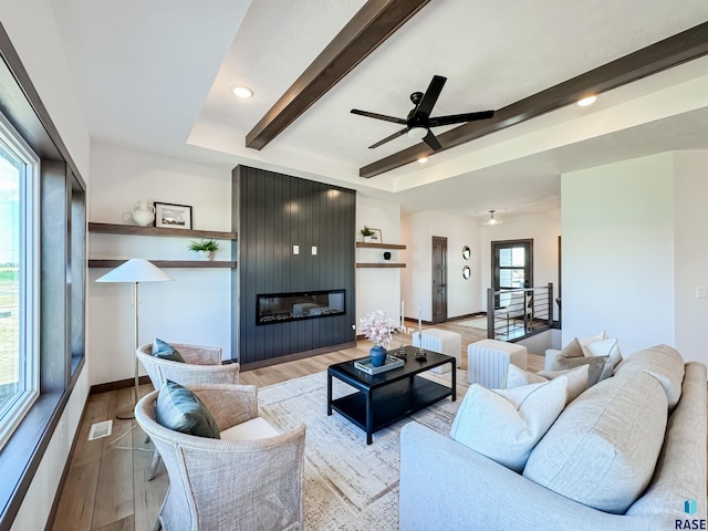 living room with visible vents, a ceiling fan, wood finished floors, a fireplace, and beam ceiling