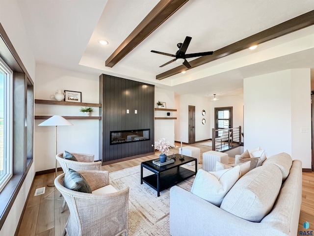 living room featuring light wood-style flooring, a large fireplace, visible vents, baseboards, and beamed ceiling