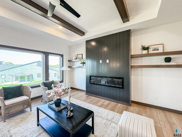 living area with a large fireplace, light wood-style flooring, baseboards, and beam ceiling