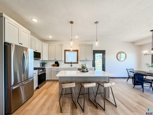 kitchen with decorative backsplash, appliances with stainless steel finishes, a kitchen breakfast bar, light countertops, and a sink