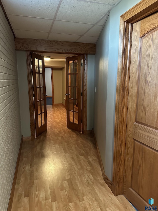 corridor with a paneled ceiling, light hardwood / wood-style flooring, brick wall, and french doors