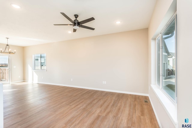 unfurnished room featuring ceiling fan with notable chandelier and light hardwood / wood-style flooring