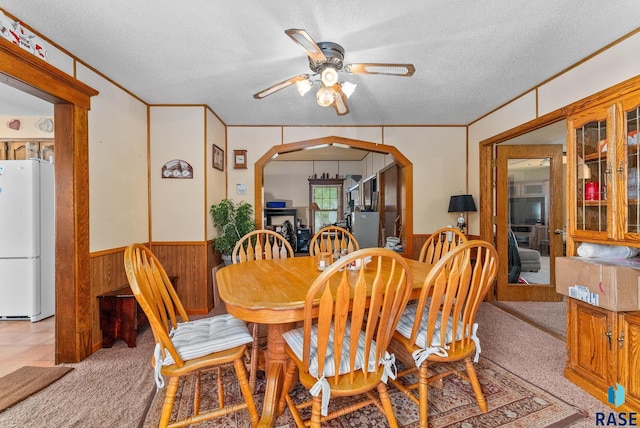 carpeted dining room with ceiling fan, wood walls, and a textured ceiling