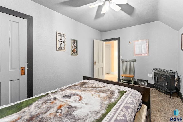 carpeted bedroom with a textured ceiling, vaulted ceiling, a wood stove, and ceiling fan