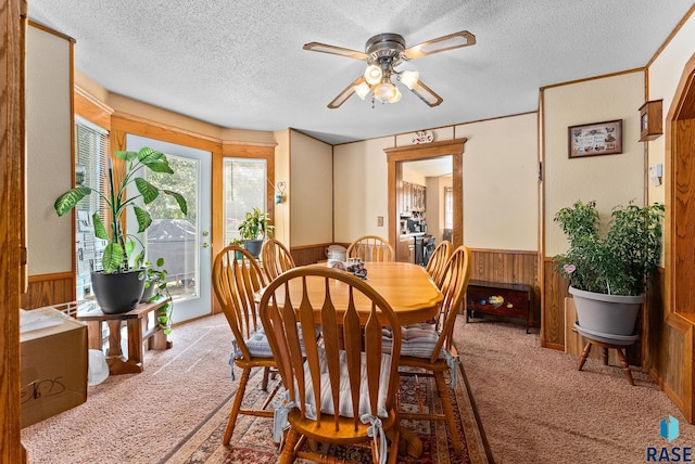 dining space featuring a textured ceiling, light colored carpet, ceiling fan, and wooden walls