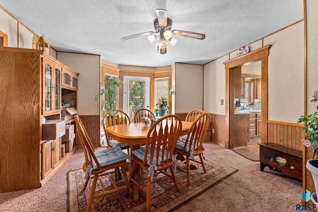 carpeted dining room with wooden walls, ceiling fan, and a textured ceiling