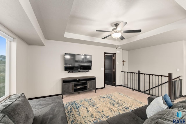 carpeted living room with a raised ceiling and ceiling fan