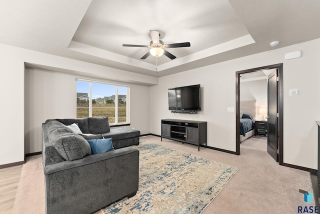 carpeted living room with a raised ceiling and ceiling fan