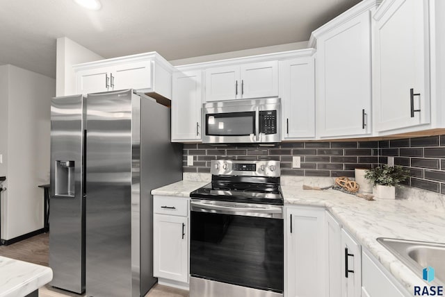 kitchen with light stone countertops, appliances with stainless steel finishes, decorative backsplash, white cabinets, and light wood-type flooring