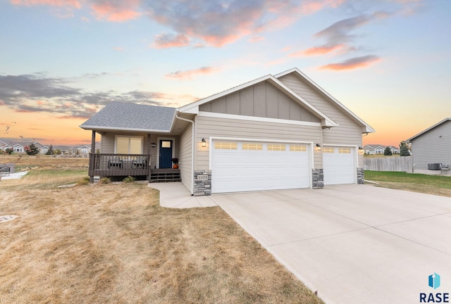 view of front of house with covered porch, a garage, central air condition unit, and a lawn