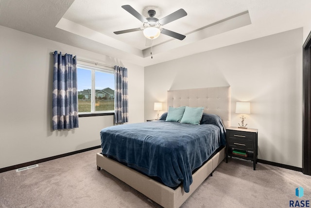 carpeted bedroom featuring ceiling fan and a tray ceiling