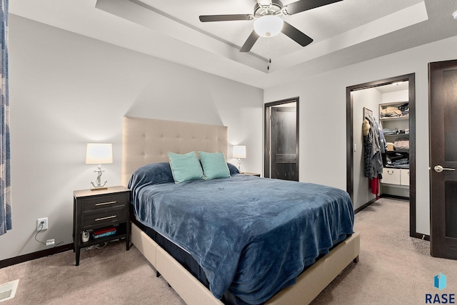 bedroom with ceiling fan, light colored carpet, and a tray ceiling