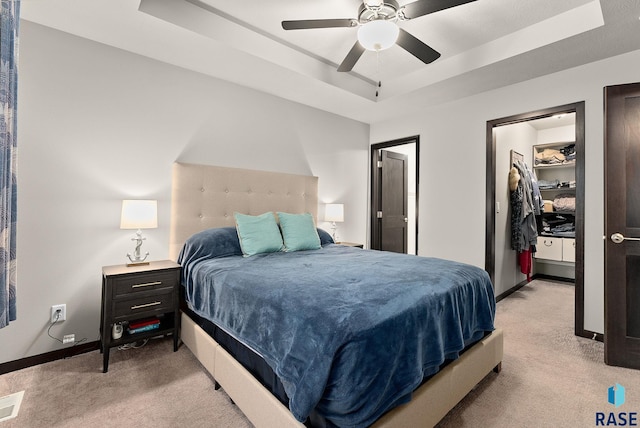 carpeted bedroom with ceiling fan, a raised ceiling, a walk in closet, and a closet