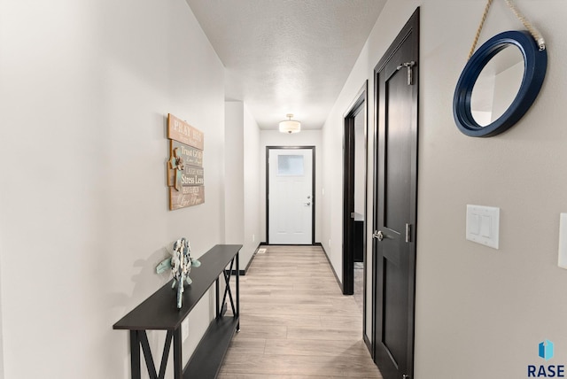 hallway with light wood-type flooring and a textured ceiling