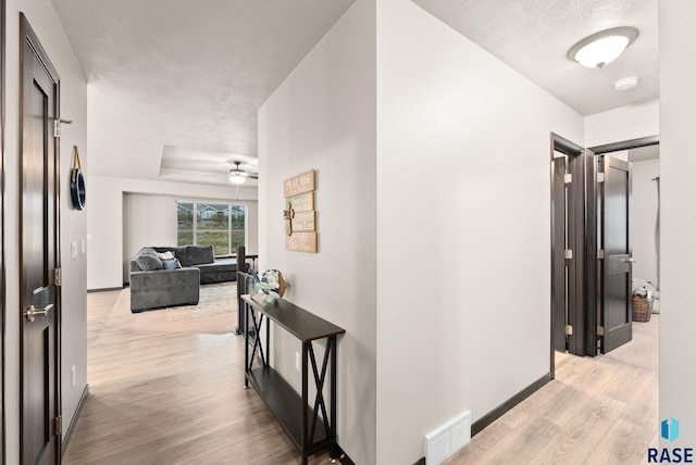 corridor featuring a raised ceiling, a textured ceiling, and light hardwood / wood-style flooring