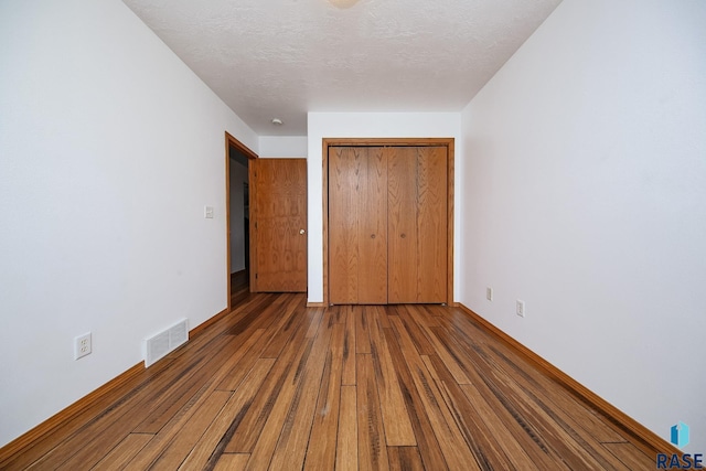 unfurnished bedroom with a textured ceiling, hardwood / wood-style flooring, and a closet