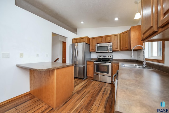 kitchen featuring sink, dark wood-type flooring, kitchen peninsula, decorative light fixtures, and appliances with stainless steel finishes