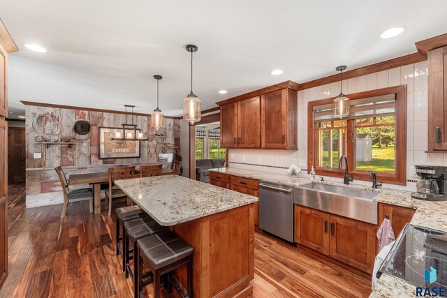 kitchen with stainless steel dishwasher, ornamental molding, pendant lighting, hardwood / wood-style floors, and a center island