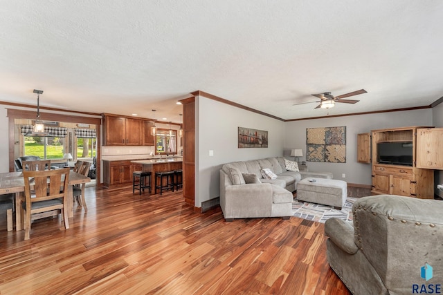 living room with a textured ceiling, light hardwood / wood-style floors, ceiling fan, and crown molding