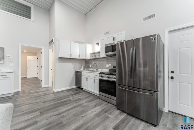 kitchen featuring appliances with stainless steel finishes, light wood-type flooring, sink, white cabinets, and a high ceiling