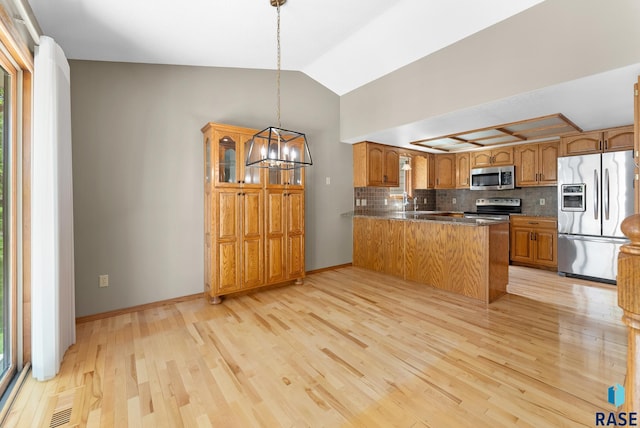 kitchen with kitchen peninsula, appliances with stainless steel finishes, vaulted ceiling, decorative light fixtures, and light hardwood / wood-style flooring